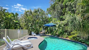 A swimming pool with two hot tubs, surrounded by lush greenery and a fenced area with lounge chairs.