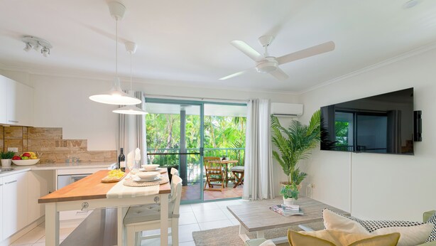 A modern kitchen with a dining area, a living room with a sofa, and a TV mounted on the wall.