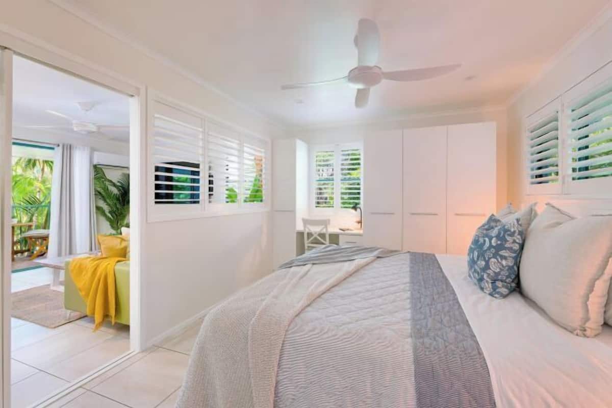 Un dormitorio con cama, ventilador de techo y vistas a un balcón con plantas.