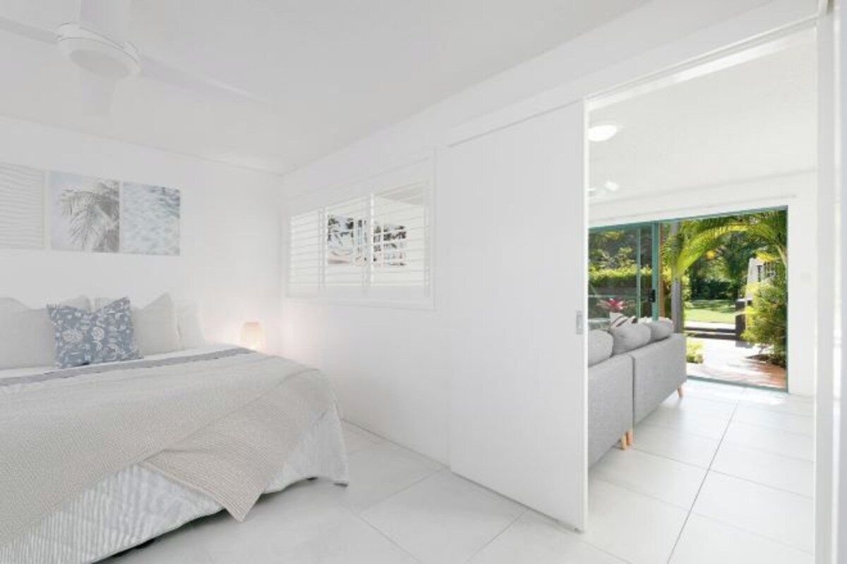 Een moderne slaapkamer met een groot bed, een bank en uitzicht op een tuin door een glazen deur.