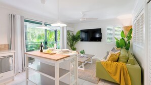 A modern kitchen with a dining table, a green sofa, and a TV mounted on the wall.