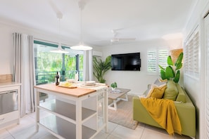 A modern kitchen with a dining table, a green sofa, and a TV mounted on the wall. - Chez Noosa Holiday Apartments (Sunshine Beach)