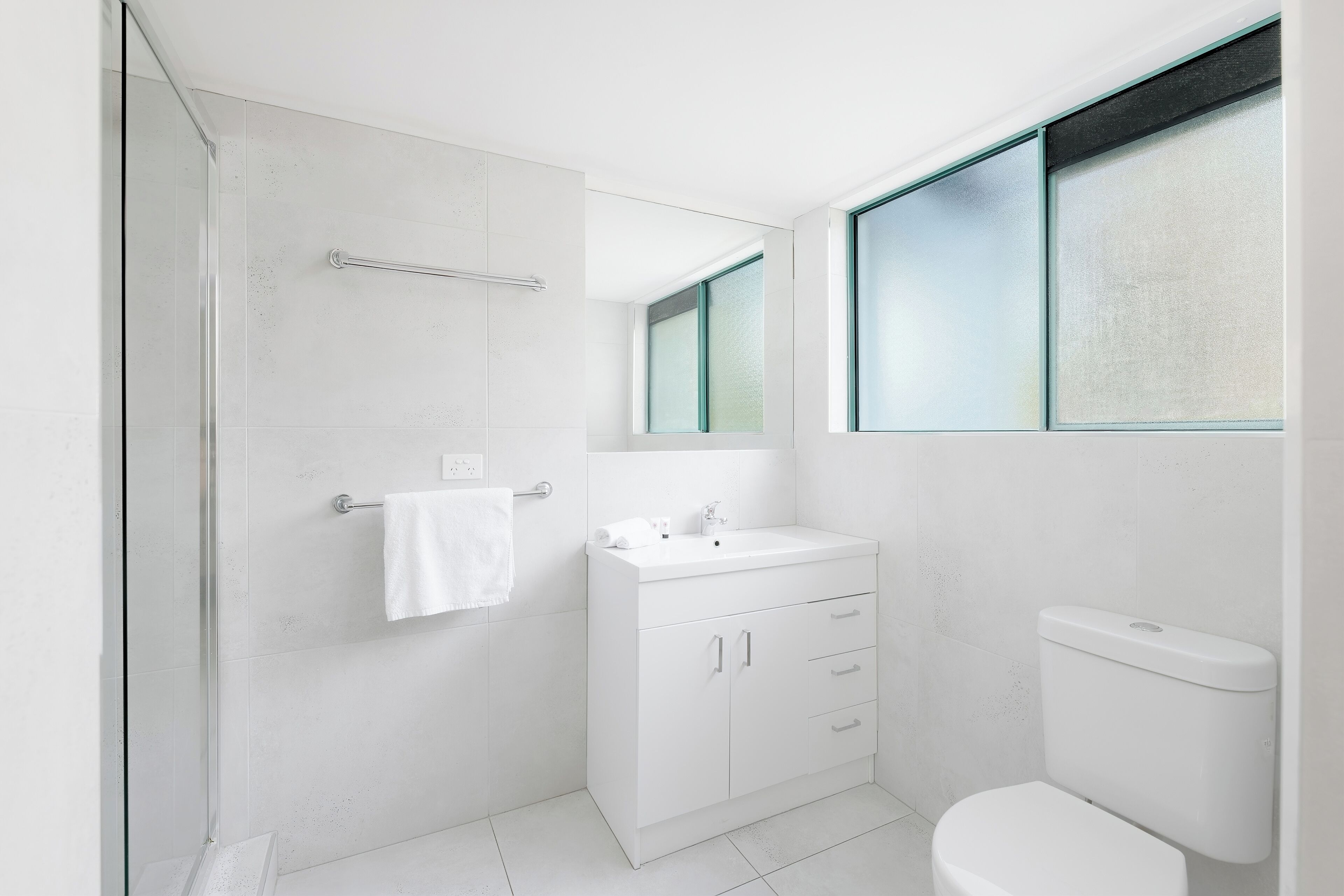Un bagno moderno con cabina doccia in vetro, lavandino bianco con specchio sopra e un water.
