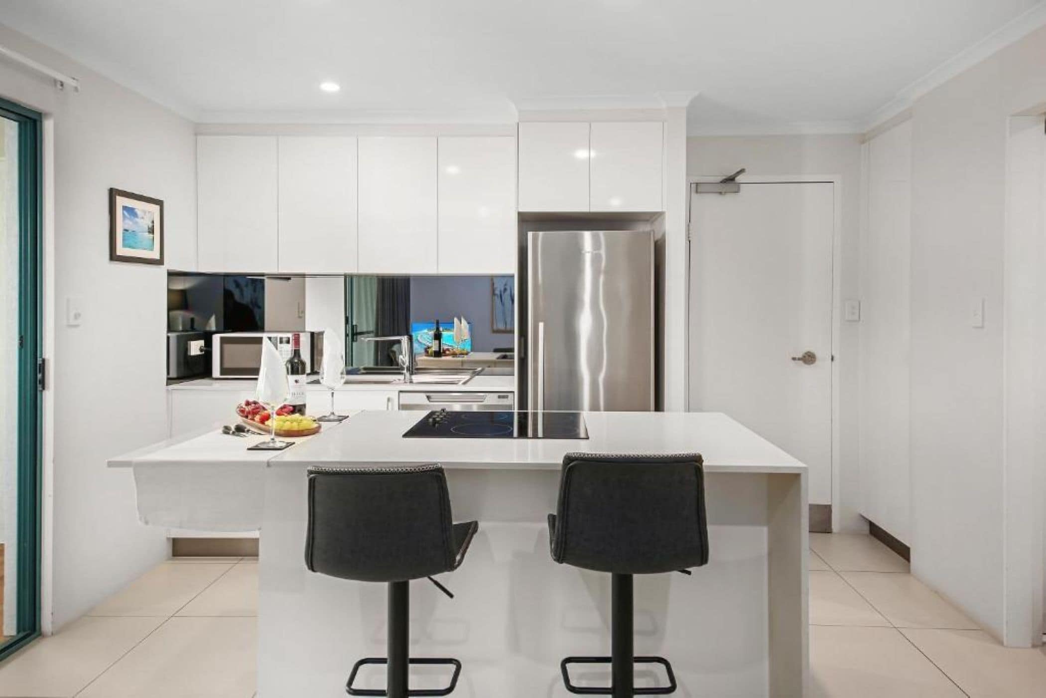 A modern kitchen with white cabinets, a stainless steel refrigerator, and a central island with two black bar stools.