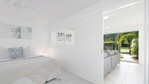 A modern bedroom with a large bed, a sofa, and a view of a garden through a glass door.