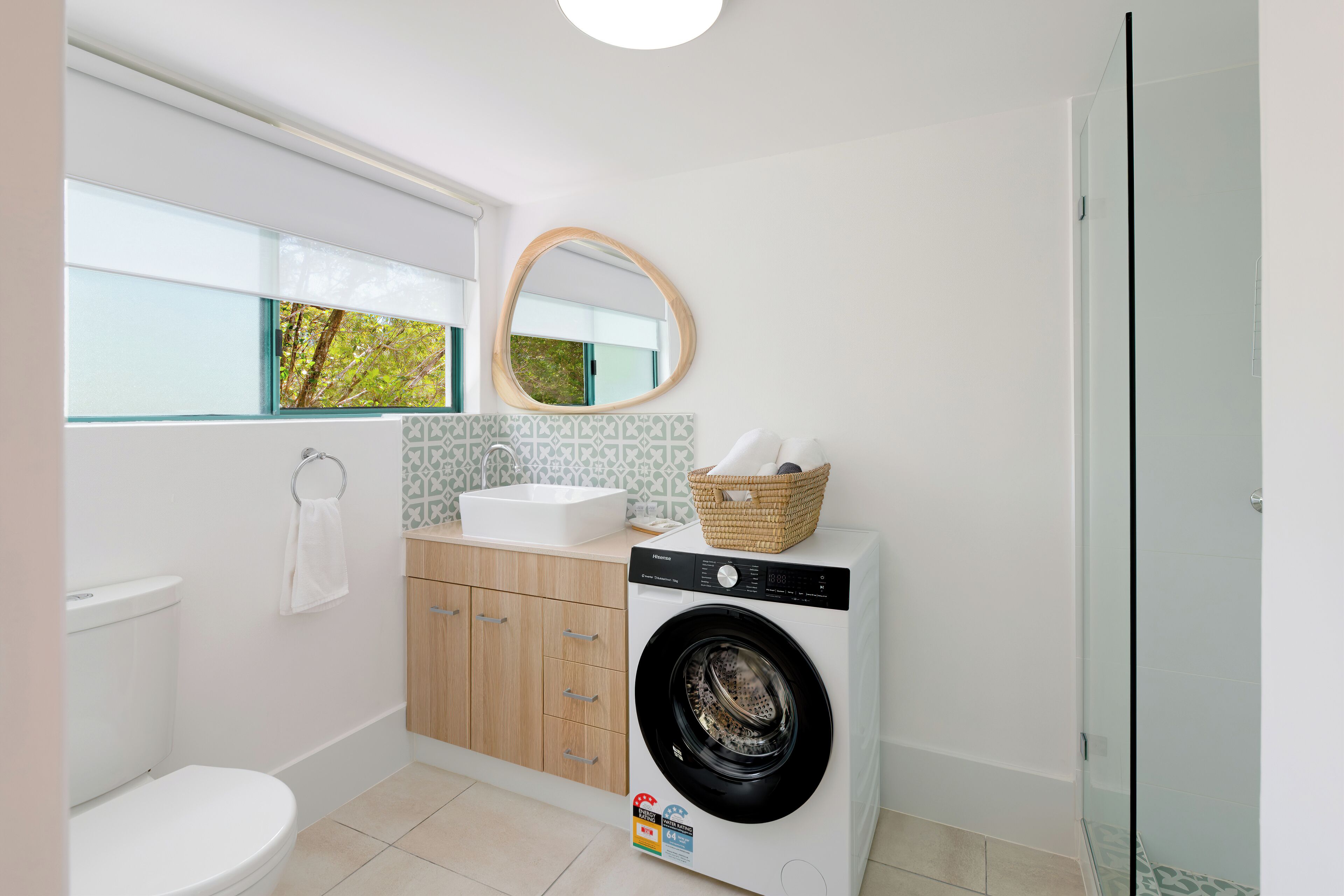 Een moderne badkamer met toilet, een wasmachine en een douchecabine met glazen wanden.