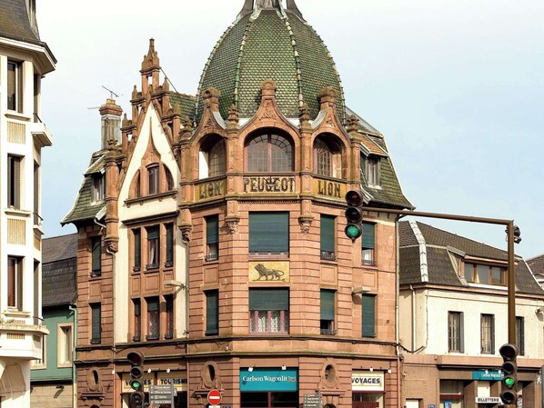 Un bâtiment historique, reconnaissable à son imposante enseigne « PEUGEOT », orné d’un emblème représentant un lion et de détails architecturaux raffinés.