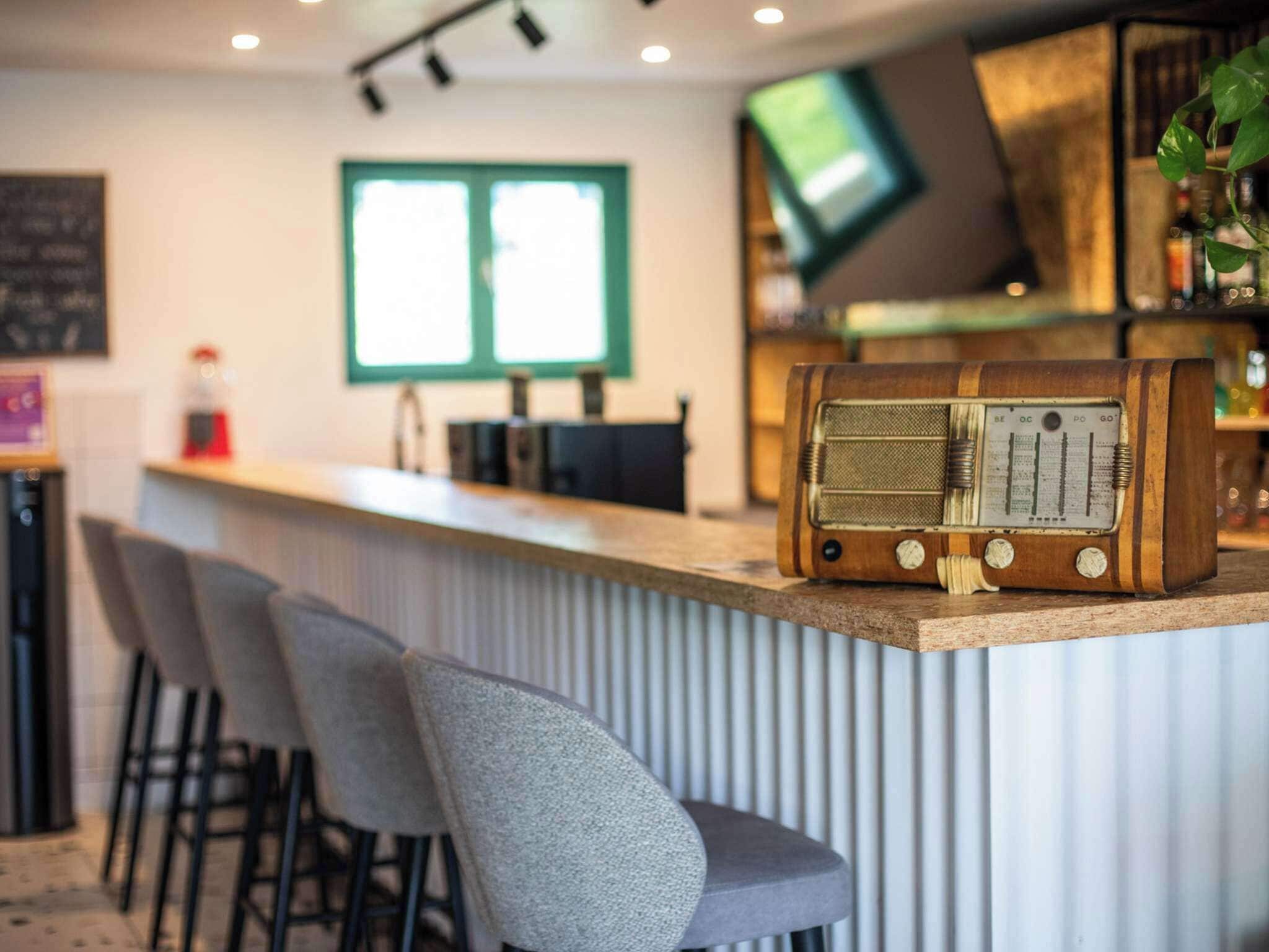 A bar area with a vintage radio, bar stools, a television, and a window with blinds.