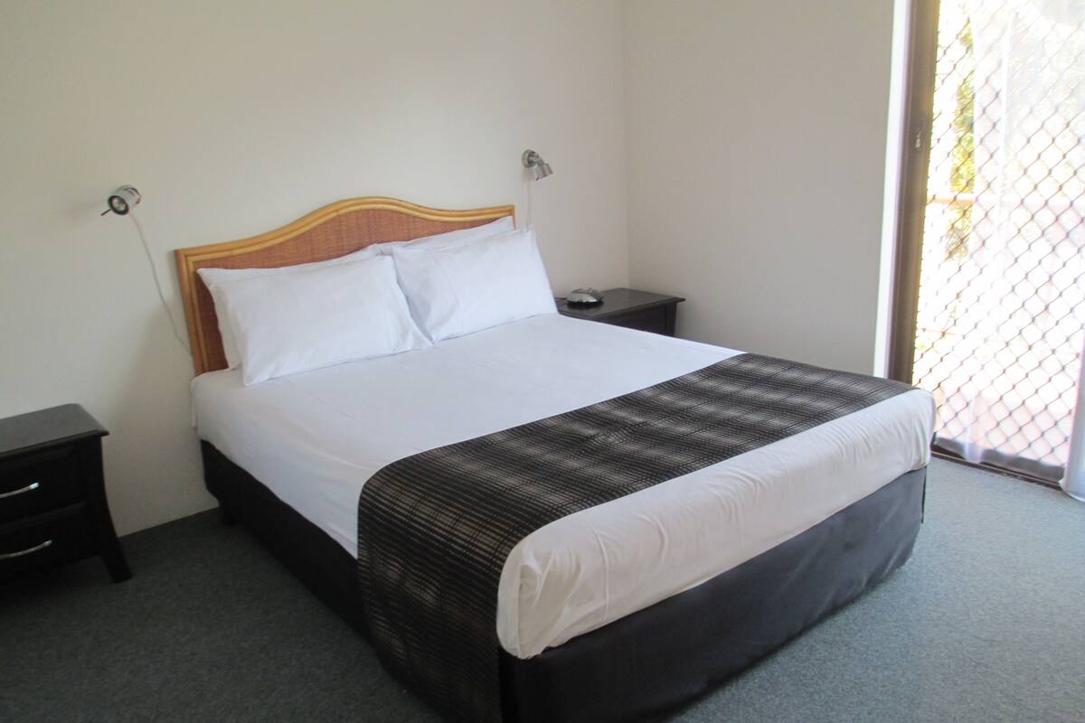A neatly made bed with a wooden headboard, a black and white patterned bedspread, and a small bedside table with a lamp.