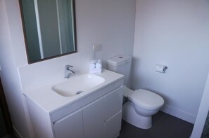 Un baño moderno con lavamanos, espejo, inodoro y mueble de almacenamiento blanco.
