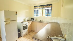 Cocina compacta con refrigerador, estufa, microondas y teléfono en la encimera.