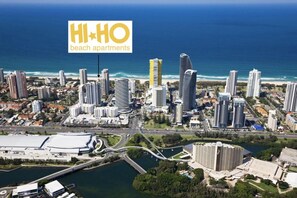 A coastal cityscape with high-rise buildings, a marina, and a large stadium. - Hi Ho Beach Apartments (Broadbeach)