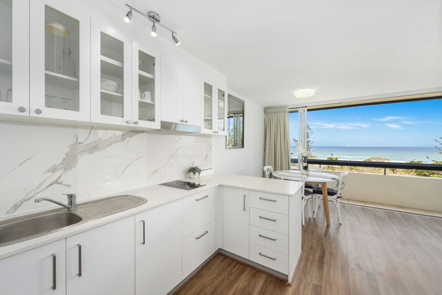 A modern kitchen with white cabinets and a view of the beach.