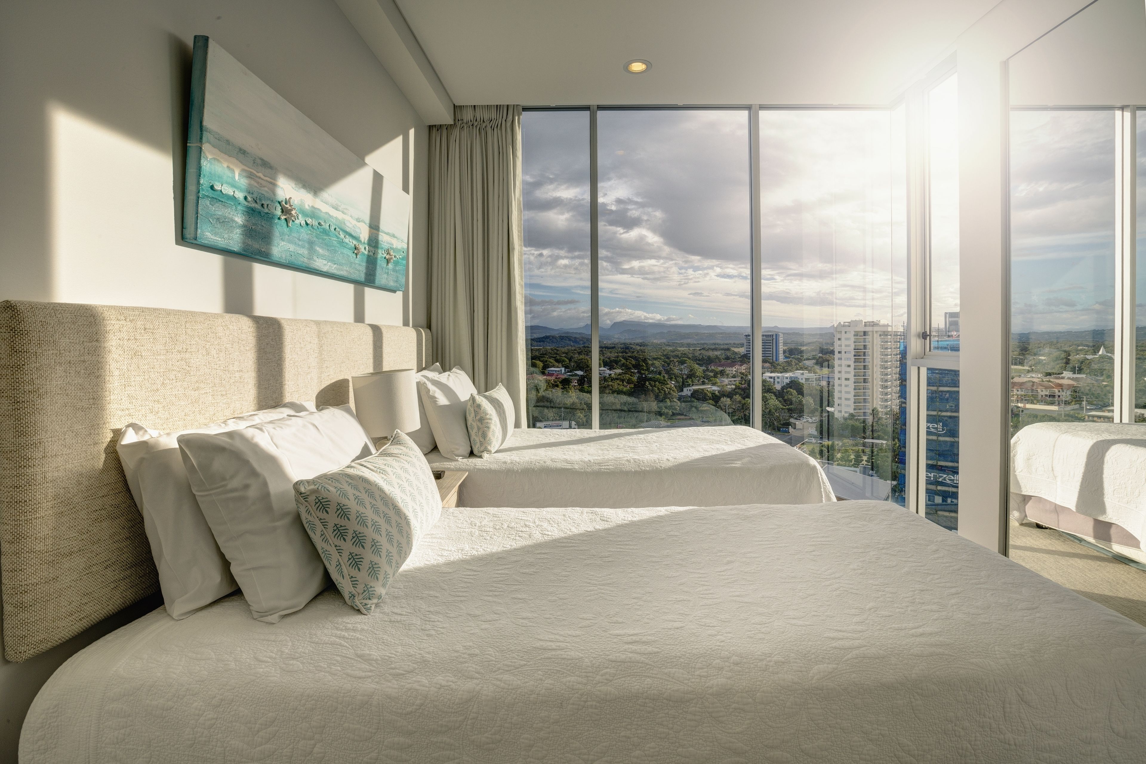 Ein Hotelzimmer mit zwei Betten, einem großen Fenster mit Blick auf die Stadt und einem Bild an der Wand.