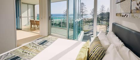 A bedroom with a large bed, a view of the ocean, and a balcony with a table and chairs.