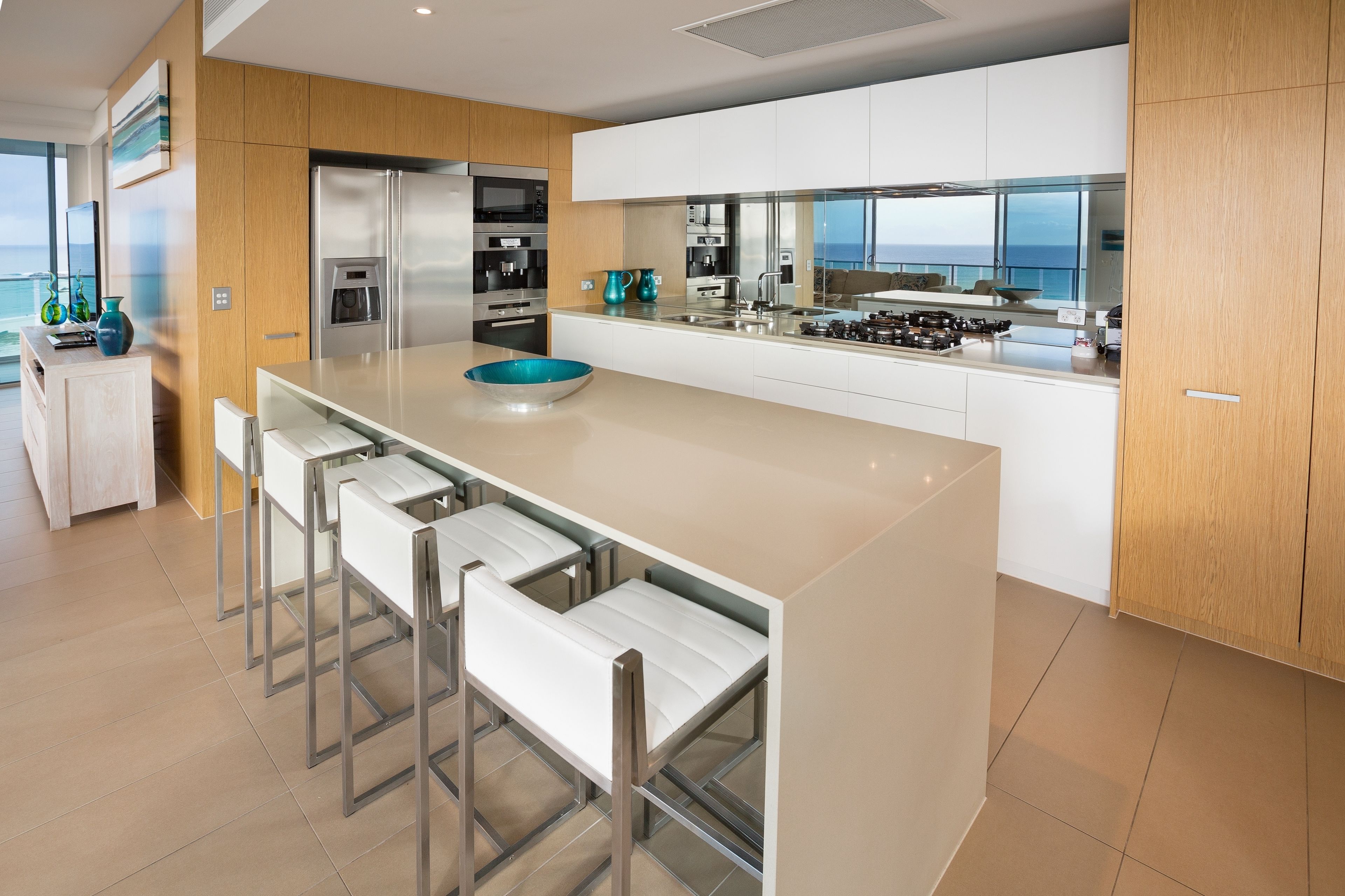 A modern kitchen with a central island, bar stools, stainless steel appliances, and a view of the ocean.