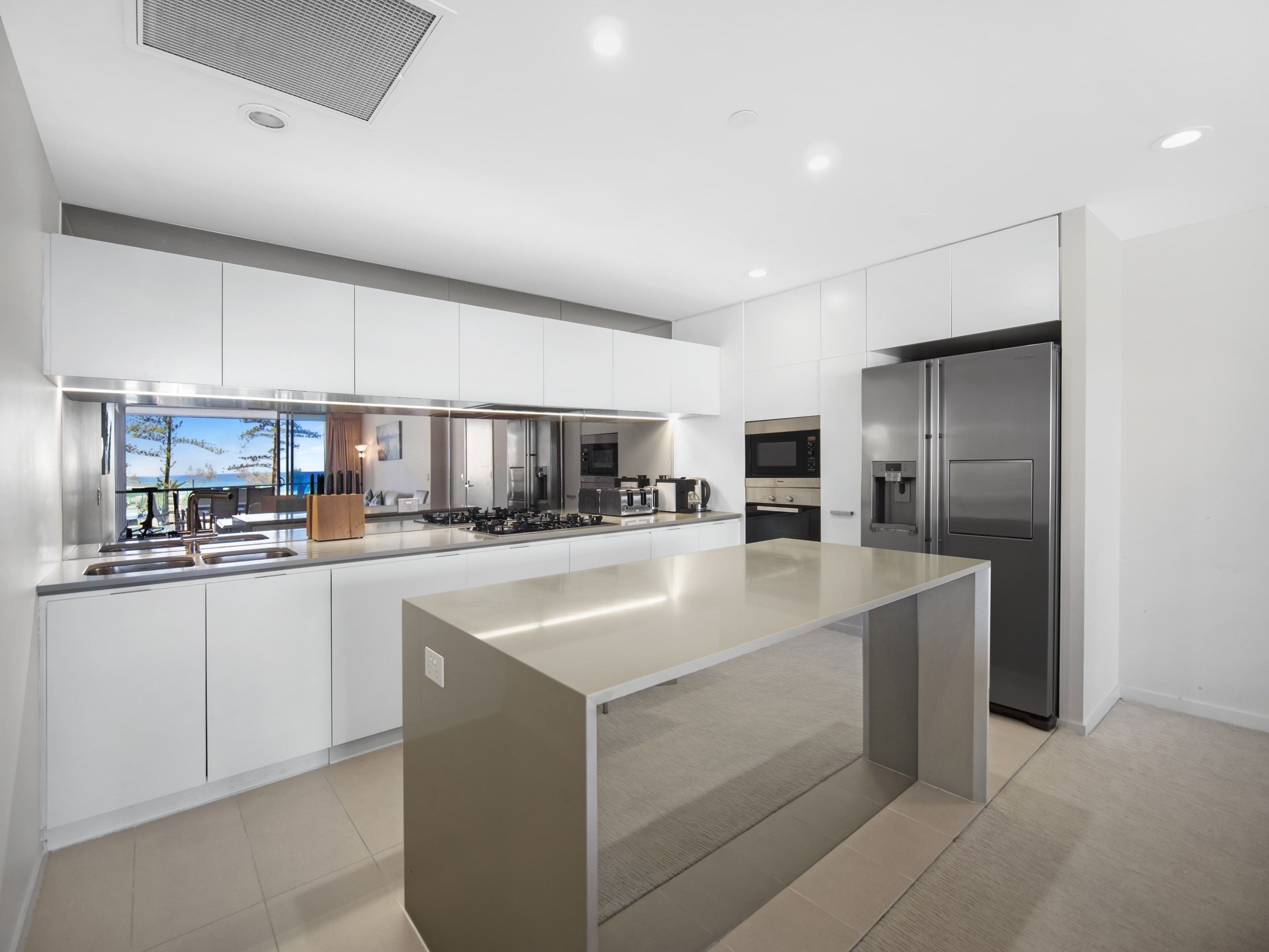 A modern kitchen with a central island, stainless steel appliances, and a view of the outdoors.