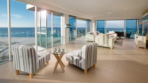 Amplia sala de estar con ventanas grandes, un conjunto de sofás, una mesa de centro y vistas al océano.