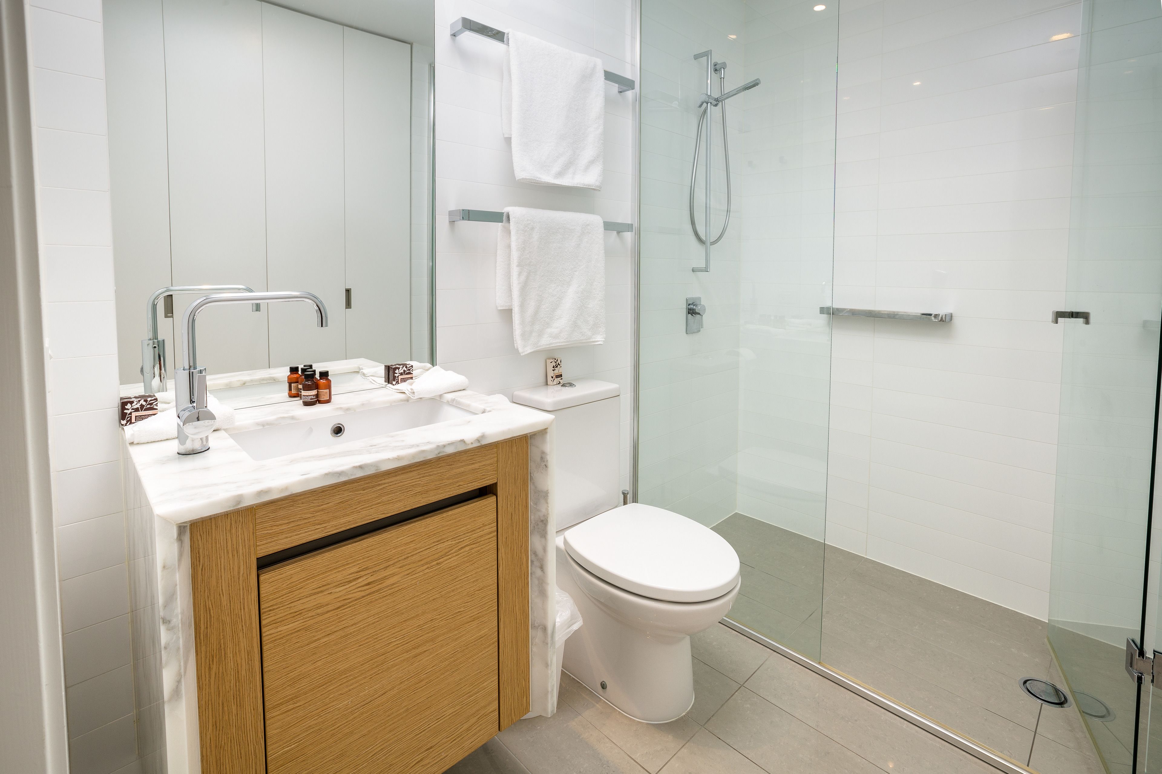 A modern bathroom with a glass shower enclosure, a white sink with a marble countertop, and a wooden vanity.