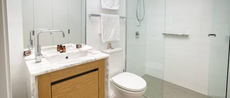 A modern bathroom with a glass shower enclosure, a white sink with a marble countertop, and a wooden vanity.