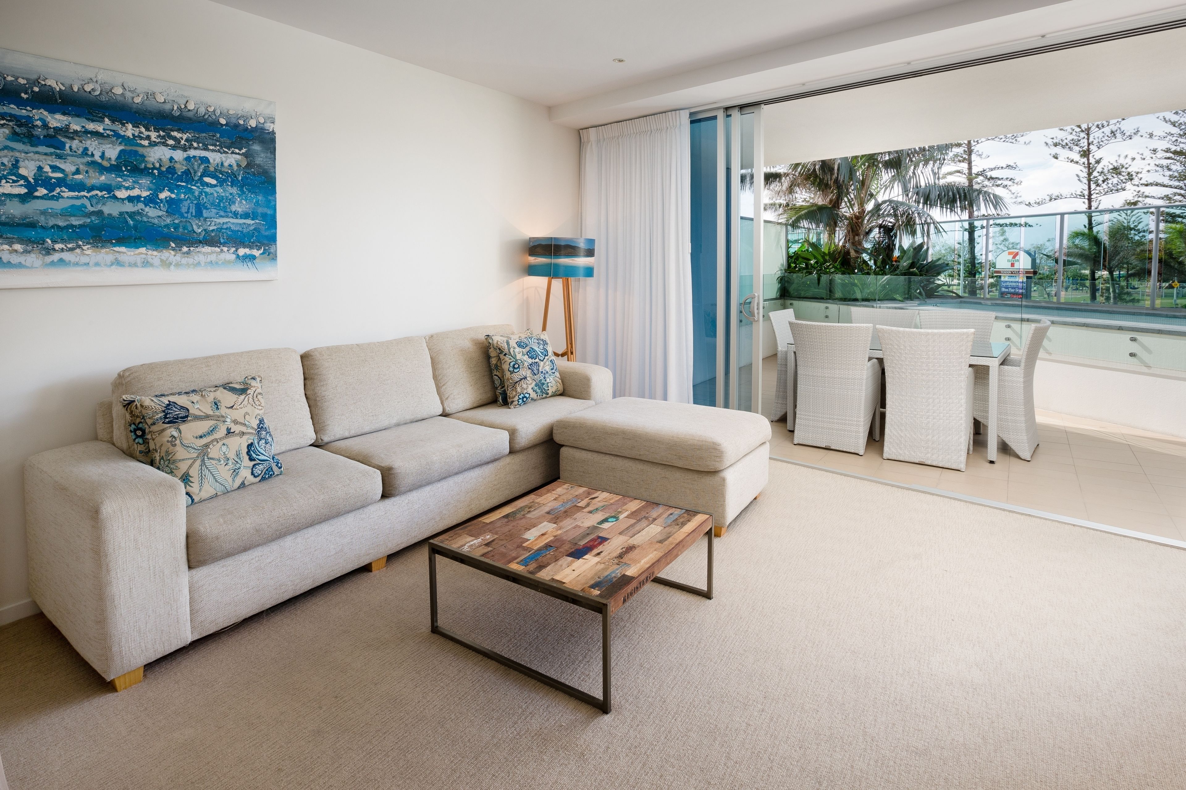 Un salon moderne avec un canapé beige, une table basse et une vue sur un balcon aménagé avec du mobilier d’extérieur.