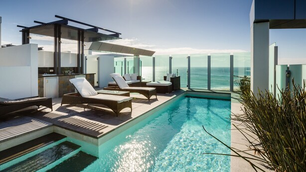 Un área de piscina moderna al aire libre con sillones de descanso y vista al océano.