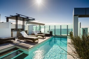 Un área de piscina moderna al aire libre con sillones de descanso y vista al océano.