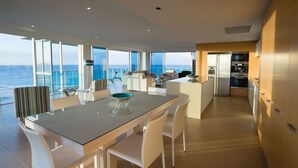 Una cocina moderna con electrodomésticos de acero inoxidable, un comedor con mesa de vidrio y ventanas amplias con vistas al océano.