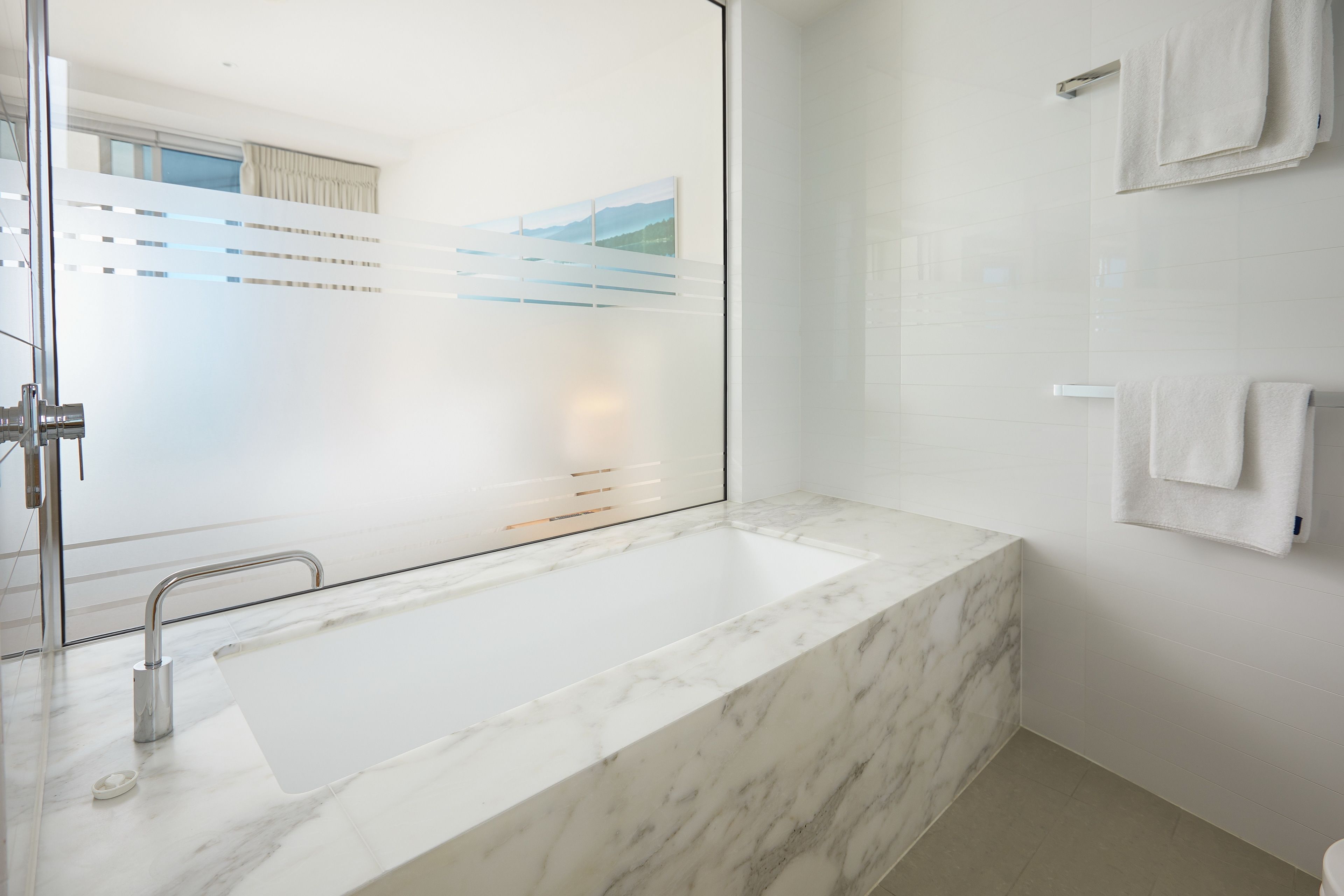 Un baño moderno con un lavamanos grande de mármol, un box de ducha de vidrio y un perchero en la pared.