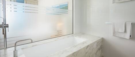 Un baño moderno con un lavamanos grande de mármol, un box de ducha de vidrio y un perchero en la pared.