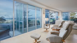 Una sala de estar moderna con amplios ventanales, un sofá, otomanas y una mesita auxiliar.