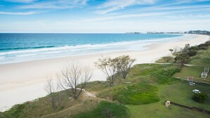 A coastal view with a beach, grassy areas, and a distant city skyline. - San Simeon Apartments (Tugun)