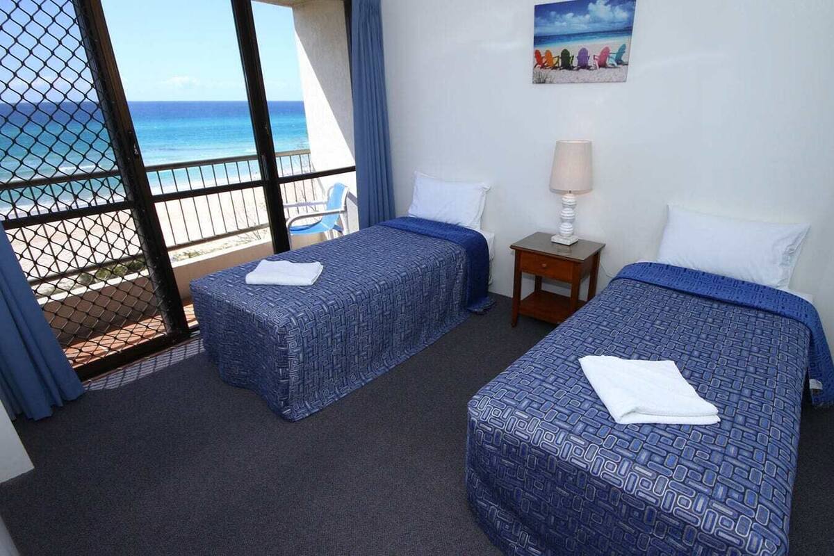 A hotel room with two beds, a nightstand, a lamp, and a view of the ocean.