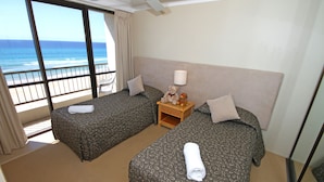 A hotel room with two beds, a nightstand with a lamp, and a view of the ocean. - San Simeon Apartments (Tugun)