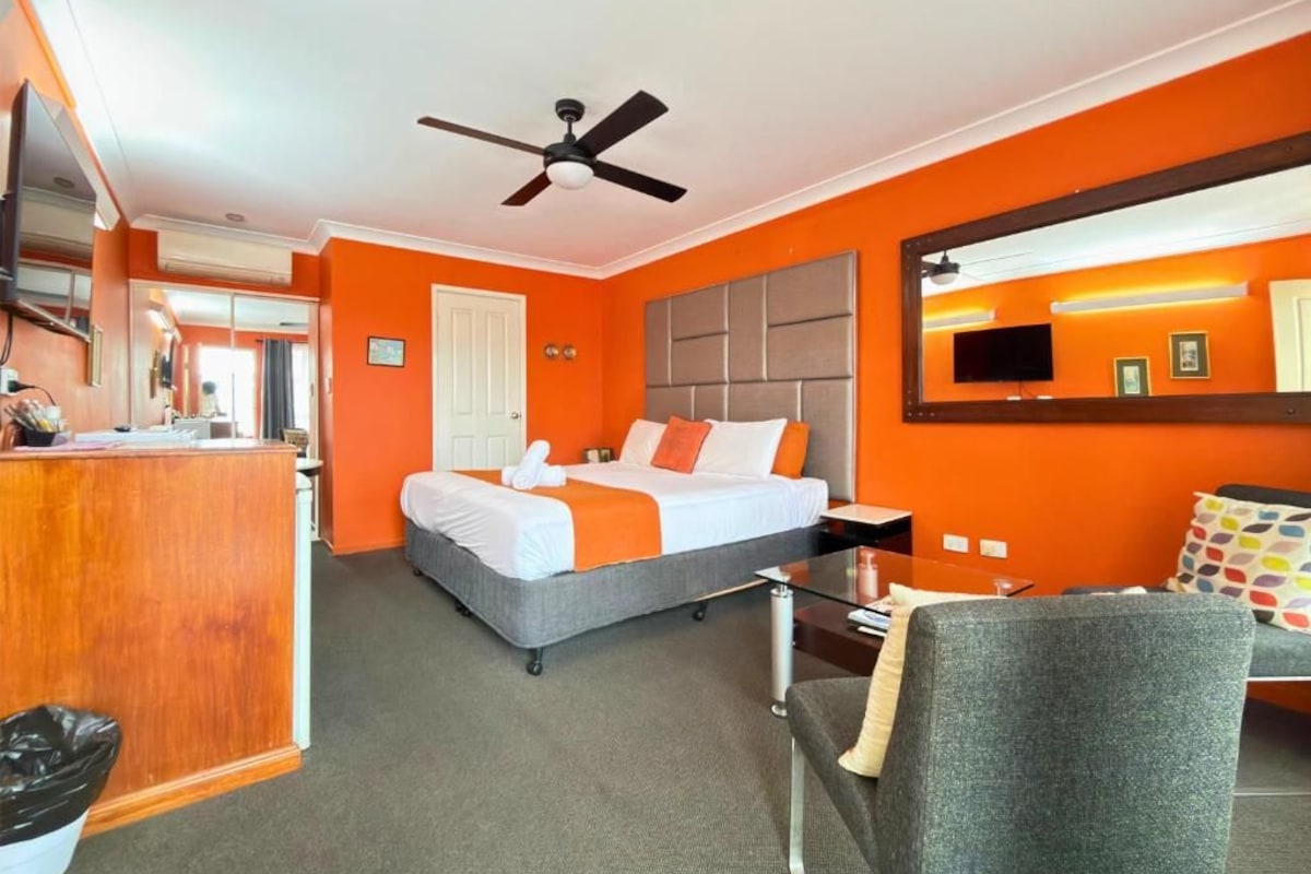 A hotel room with a bed, desk, chair, and a ceiling fan.