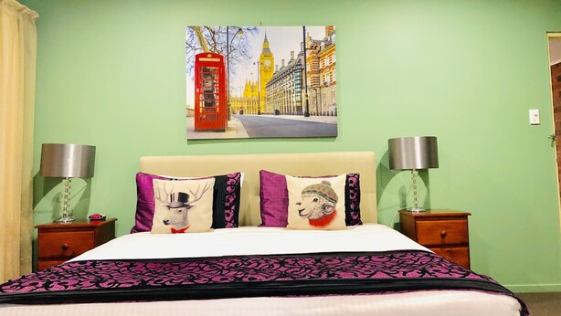 A bed with a white headboard, two bedside tables with lamps, and a painting of a red telephone booth and a clock tower on the wall. - Aussie Rest Motel (Cessnock)