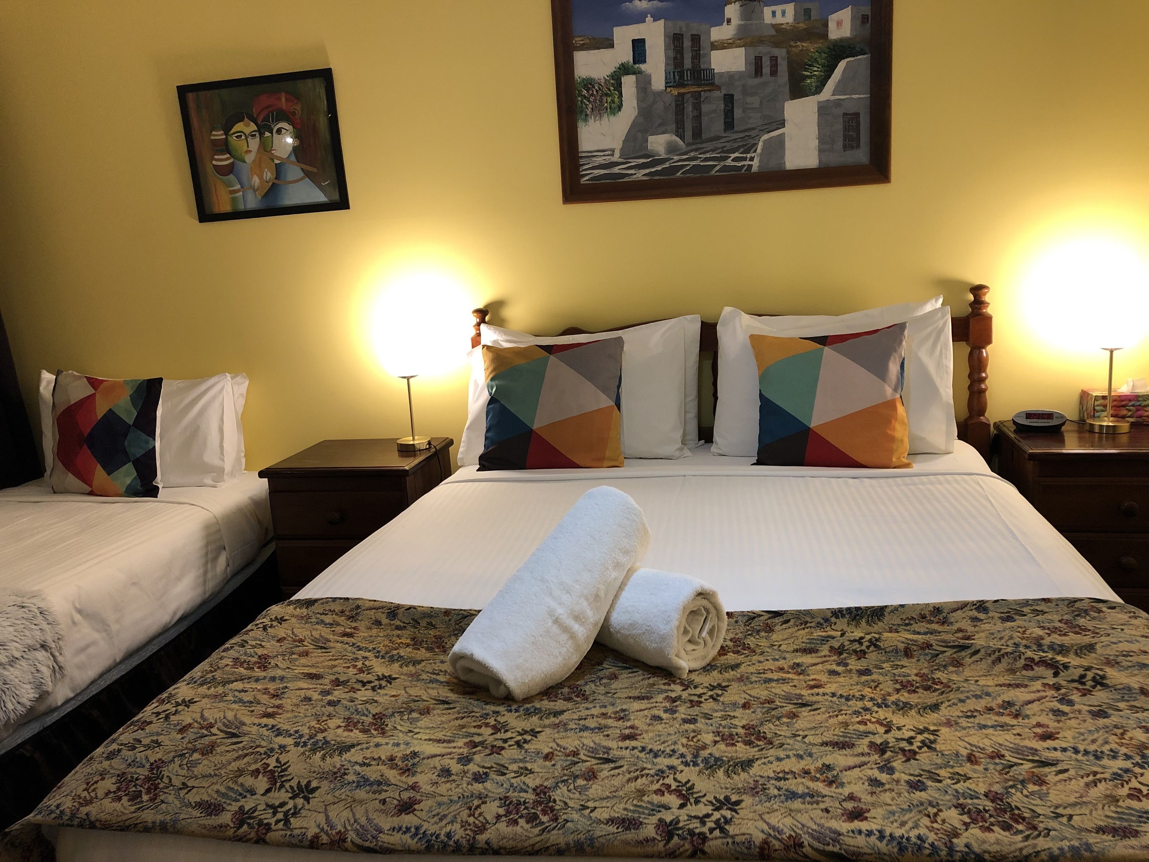Ein Hotelzimmer mit zwei Betten, einer zart gemusterten Tagesdecke und einem Gemälde einer Küstenlandschaft.