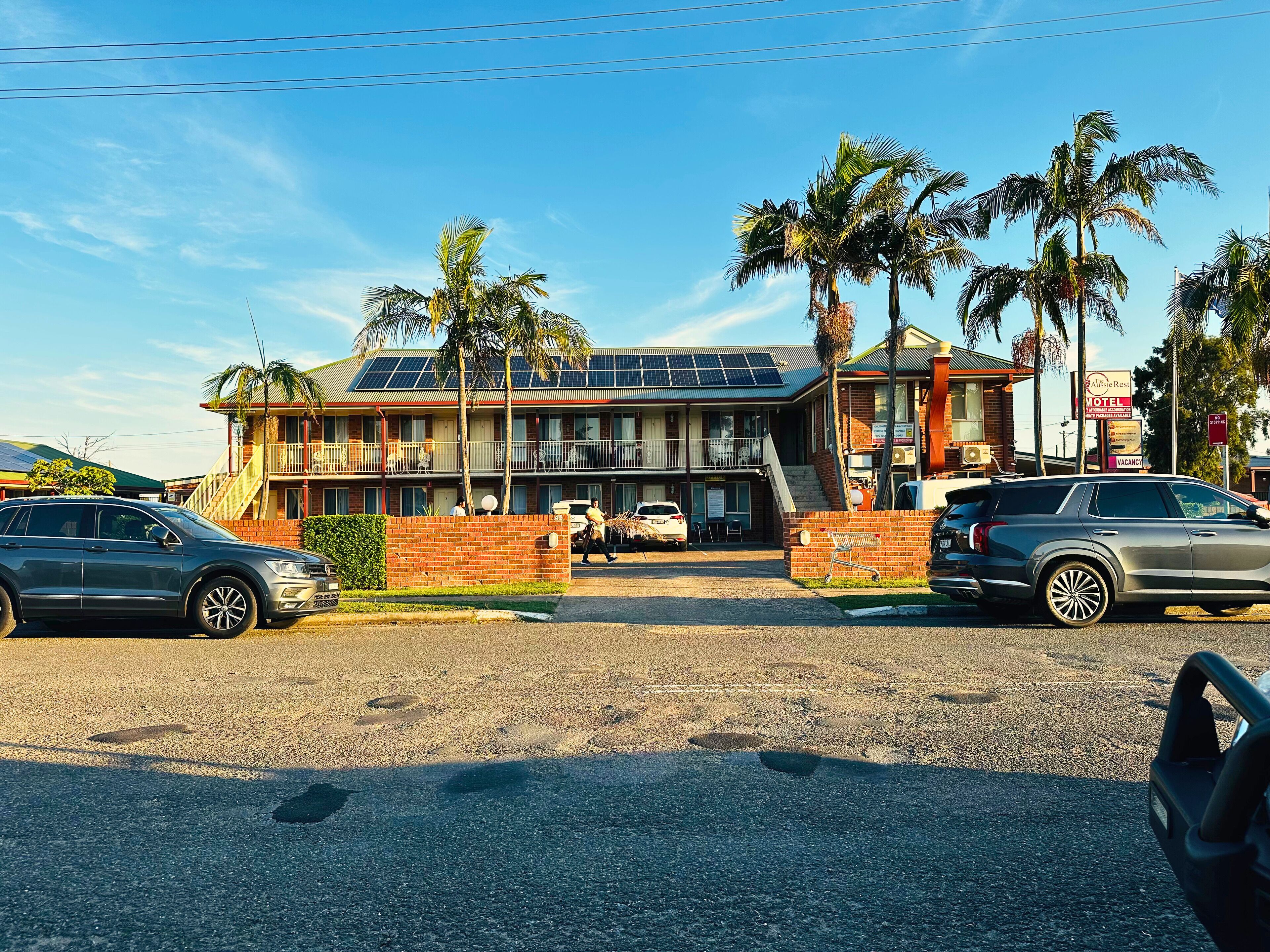 A motel with a two-story building, solar panels on the roof, and a sign advertising the All's Rest Motel.