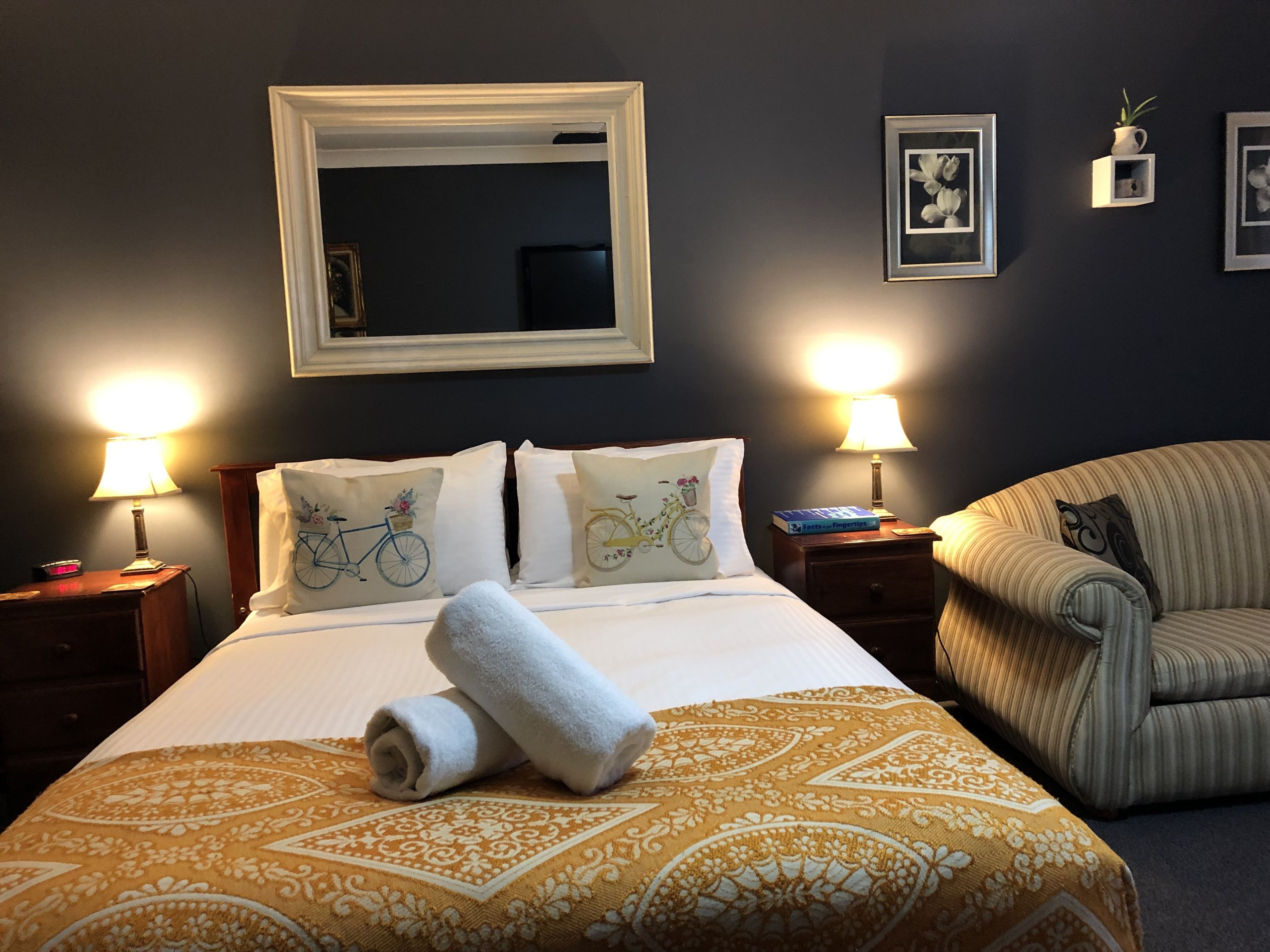 A hotel room with a bed, two bedside lamps, a chair, and framed pictures on the wall.