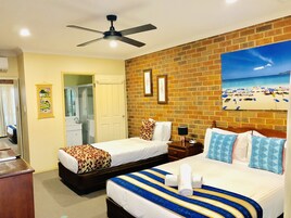 A hotel room with two beds, a ceiling fan, a bathroom with a mirror, and a beach view painting on the wall.