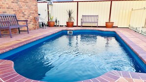 A rectangular swimming pool with a brick border, surrounded by a fence and potted plants. - Aussie Rest Motel (Cessnock)