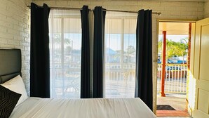 A bedroom with a large bed, a window with black curtains, and a view of a parking area outside. - Aussie Rest Motel (Cessnock)