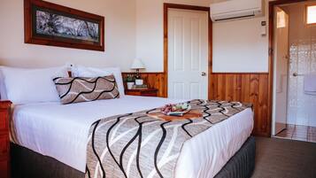 A neatly made bed with a patterned bedspread, a bedside table with a lamp, and a framed picture on the wall.