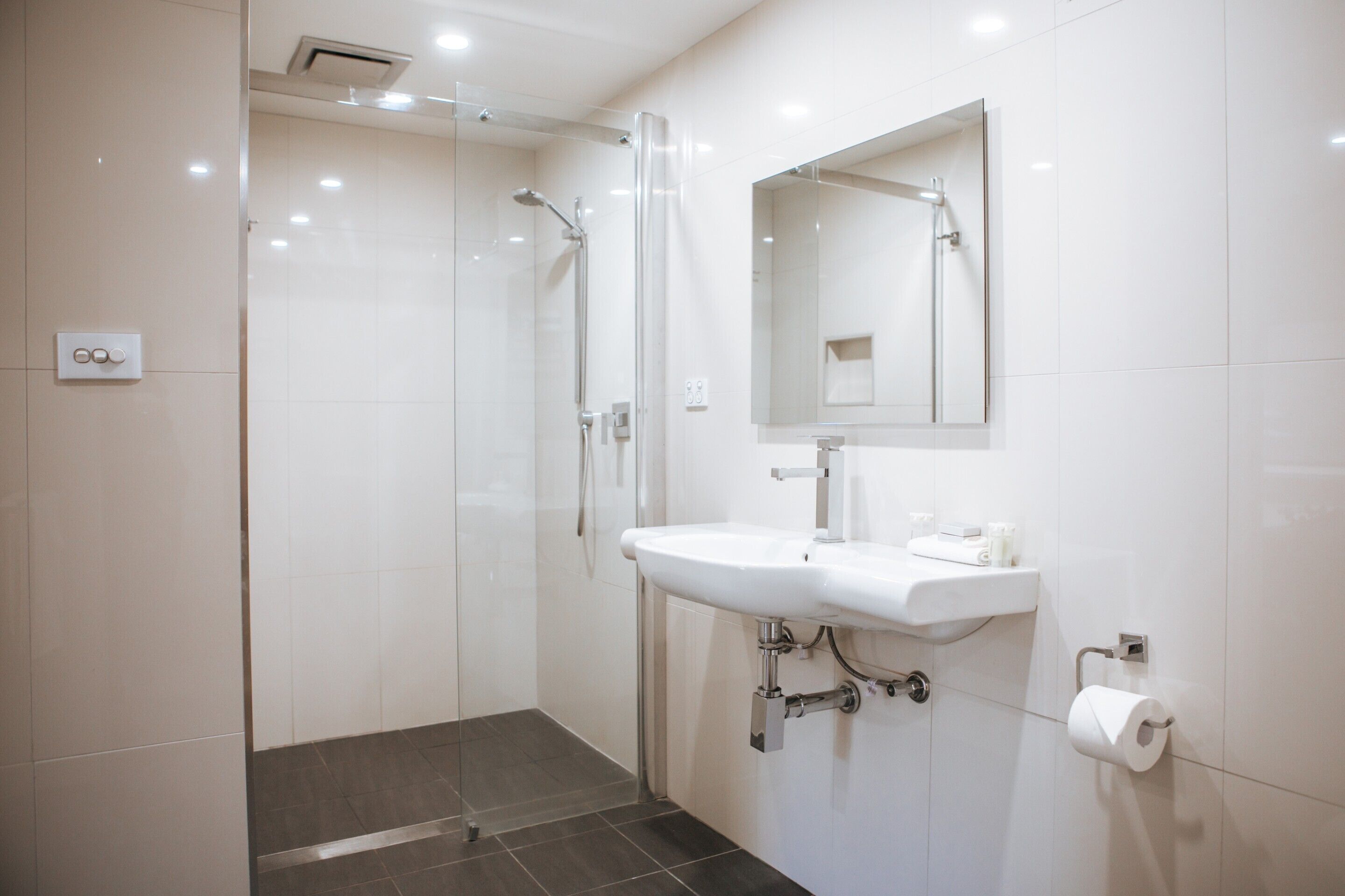 Un baño moderno con cabina de ducha de vidrio, un lavamanos blanco y un espejo encima.