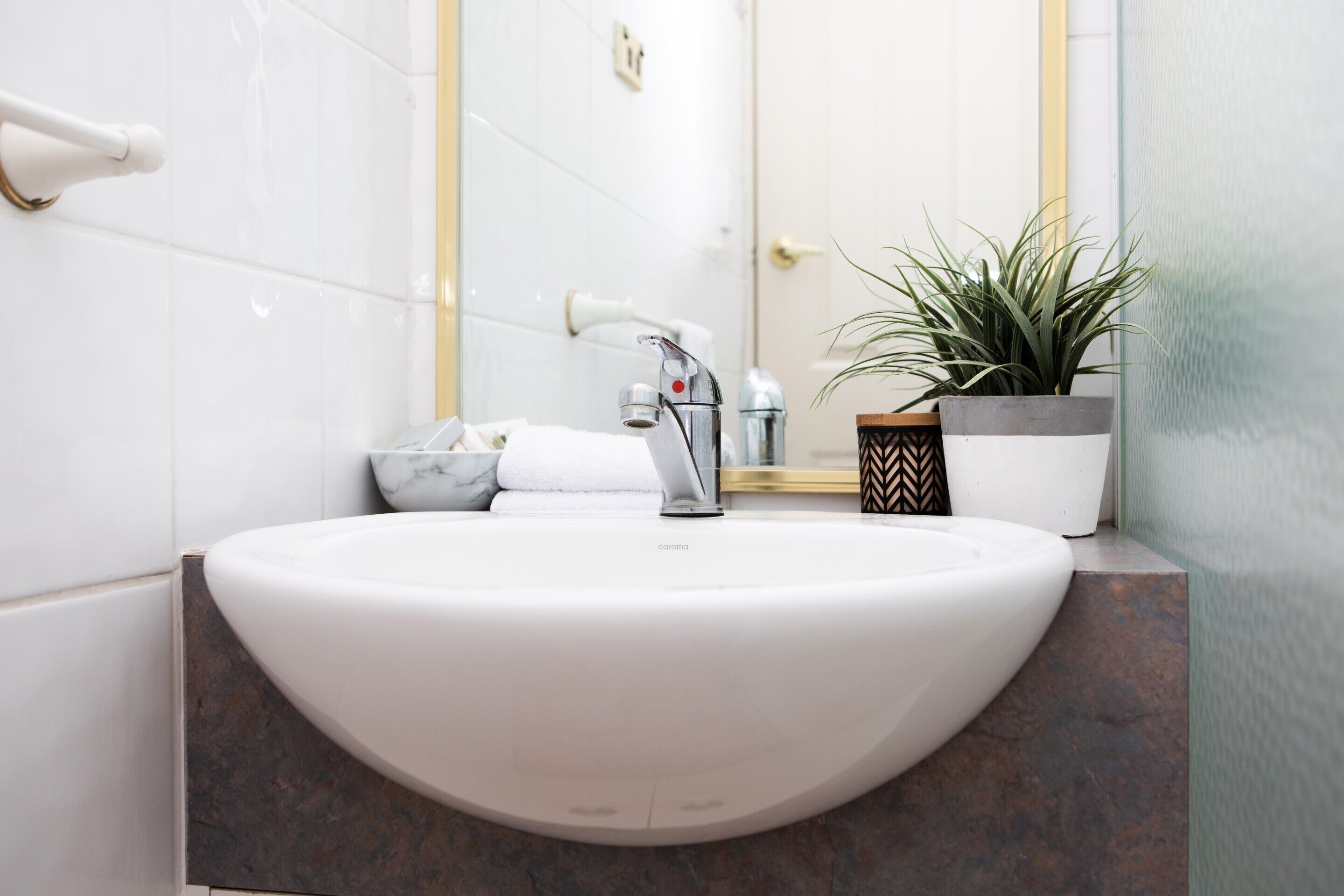 A modern bathroom with a white sink, marble countertop, and a potted plant.