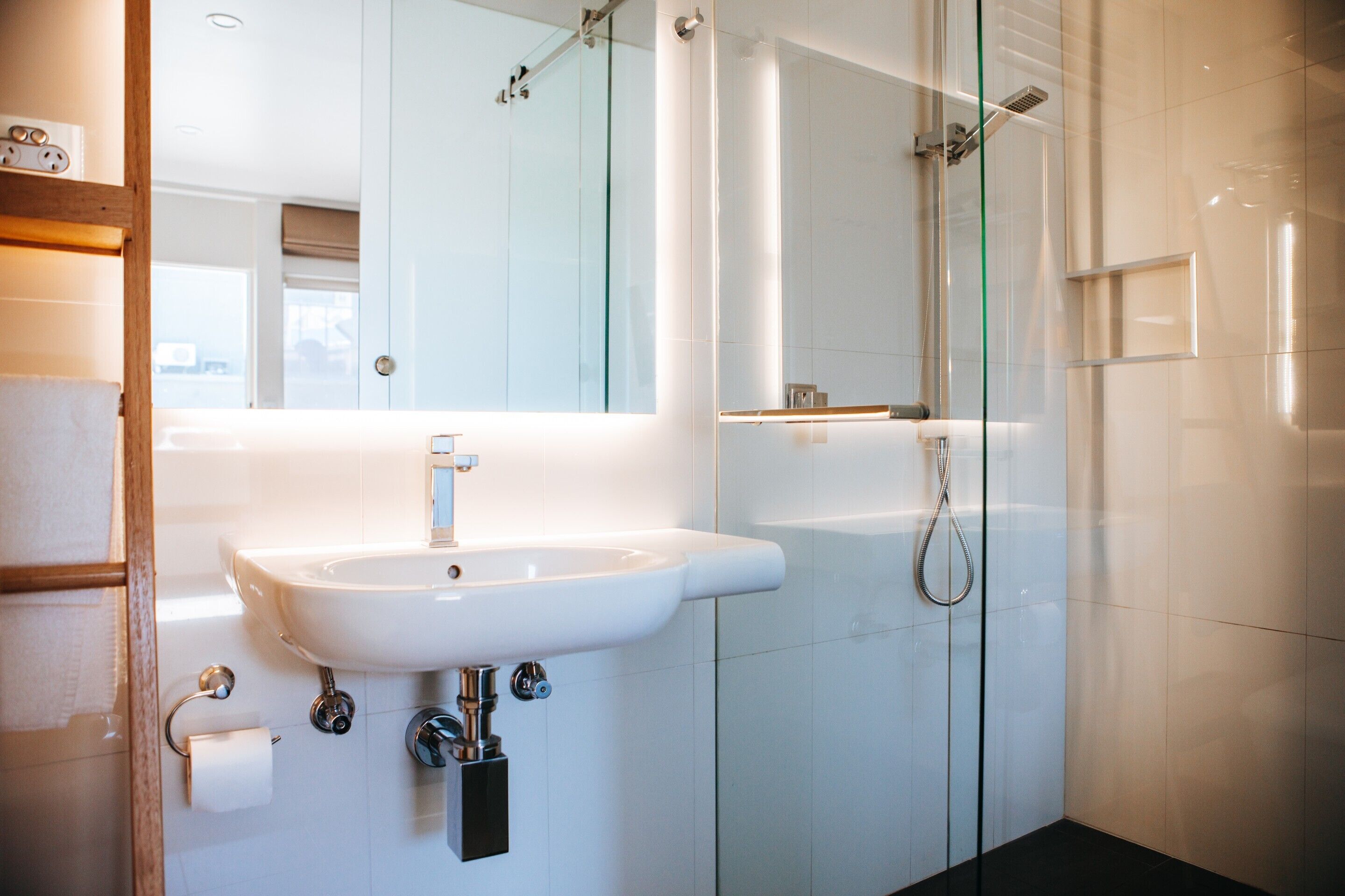 A modern bathroom with a white sink, a glass shower enclosure, and a mirror above the sink.