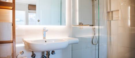 A modern bathroom with a white sink, a glass shower enclosure, and a mirror above the sink.