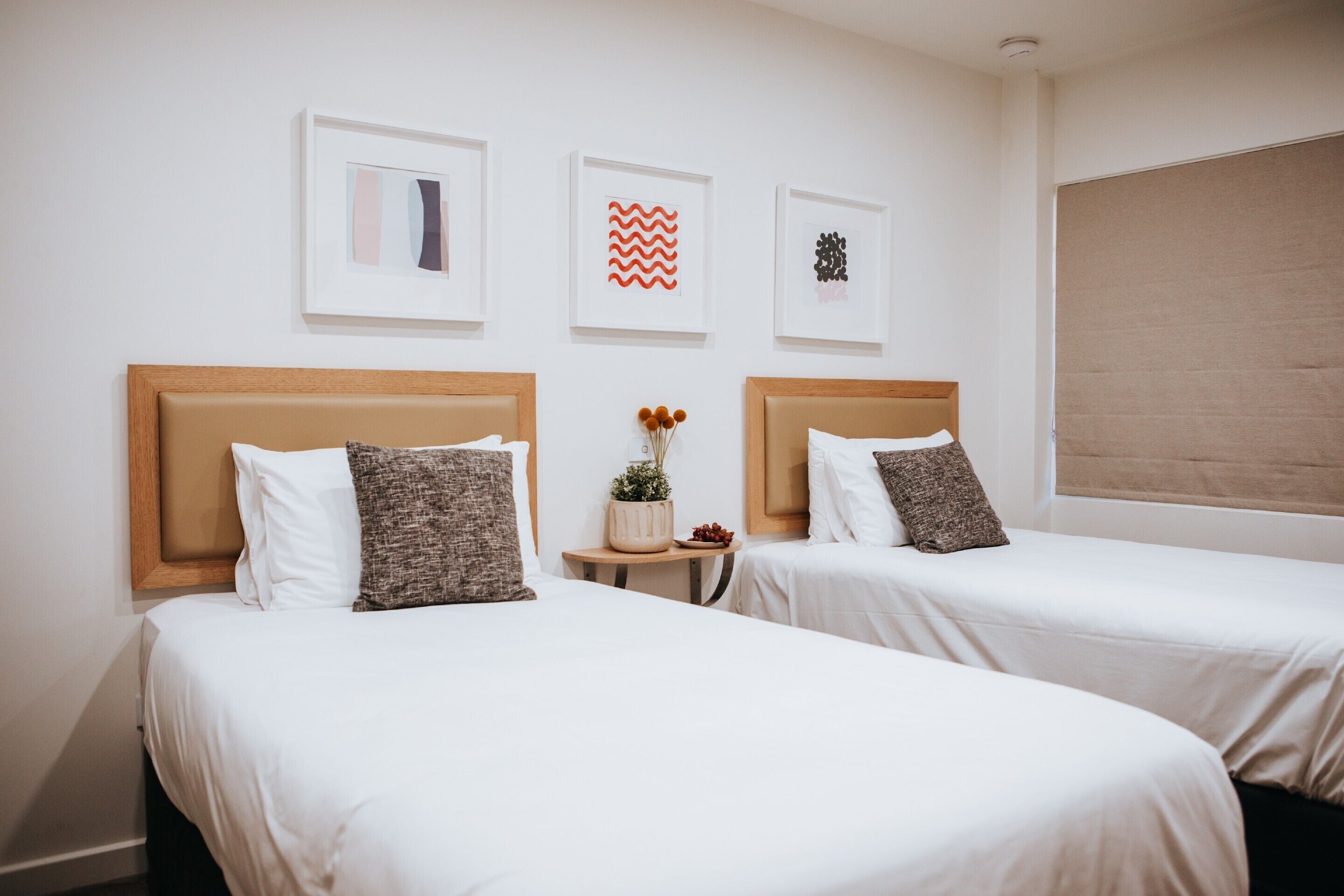 A hotel room with two beds, white bedding, wooden headboards, and framed artwork on the wall.