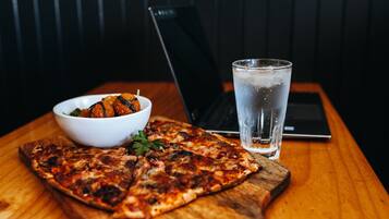 A pizza on a wooden board, a glass of water, and a bowl of food on a table.
