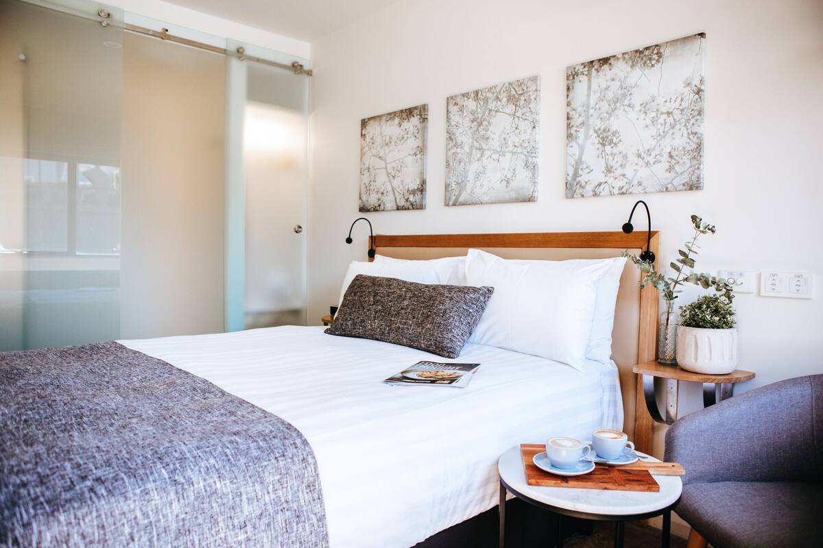 Une chambre d’hôtel avec un lit, une table de chevet sur laquelle se trouve une tasse de café et une chaise.
